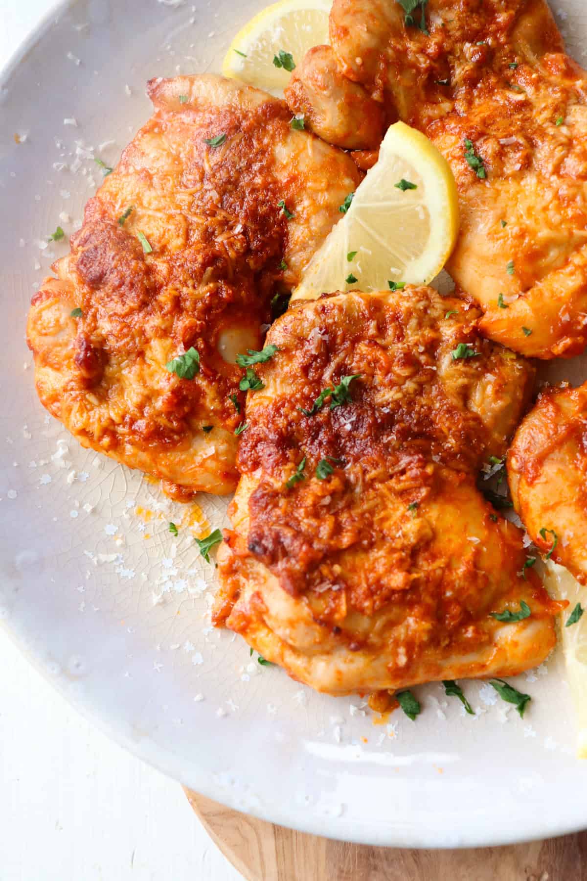 parmesan garlic chicken thighs on a plate with a slice of lemon.