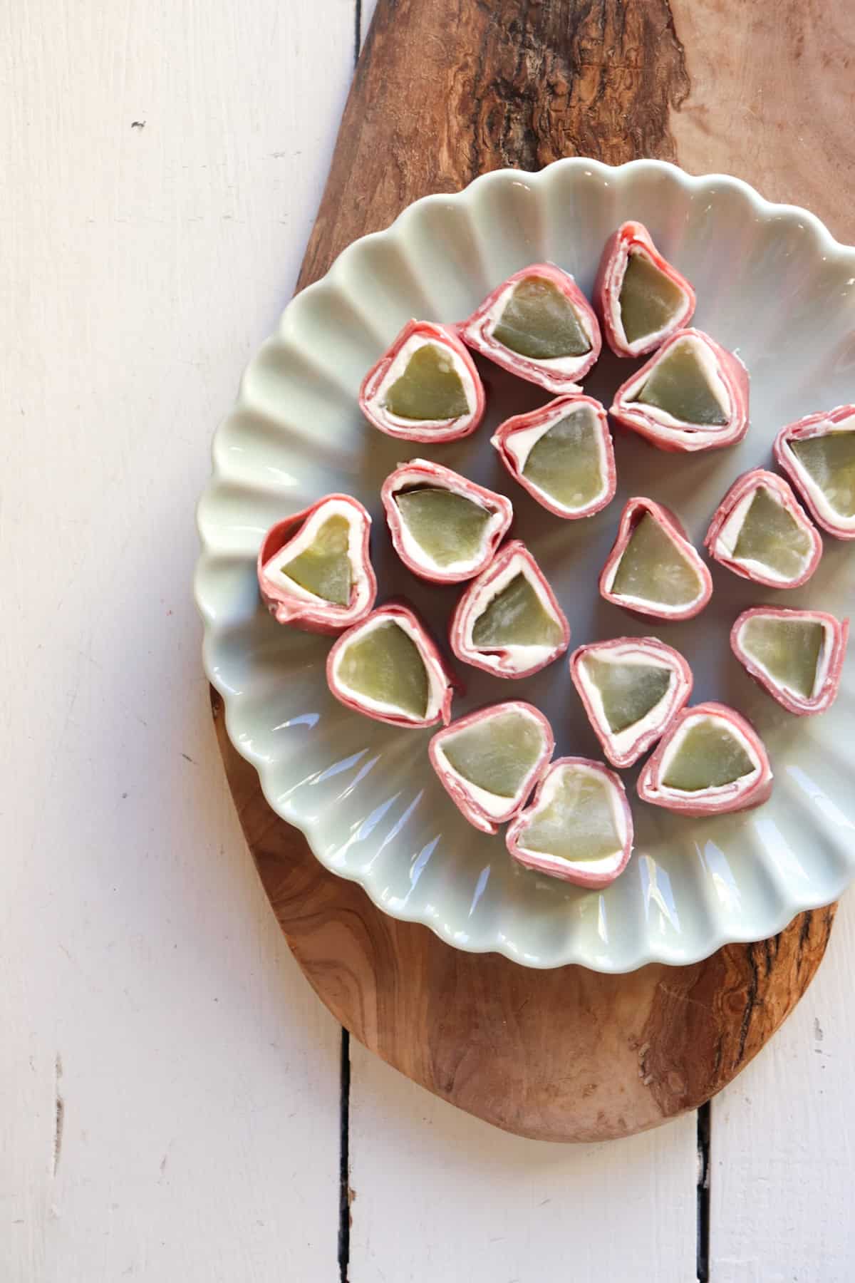 a plate of pickle roll ups on a wooden board.