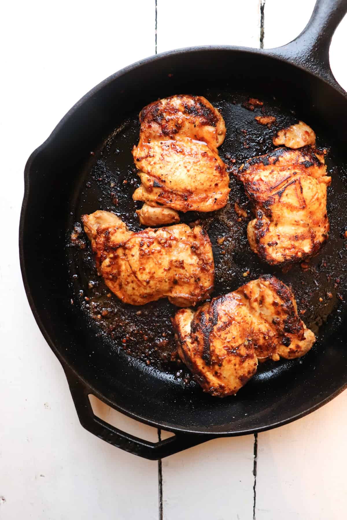 four chicken thighs cooking in a cast iron skillet.