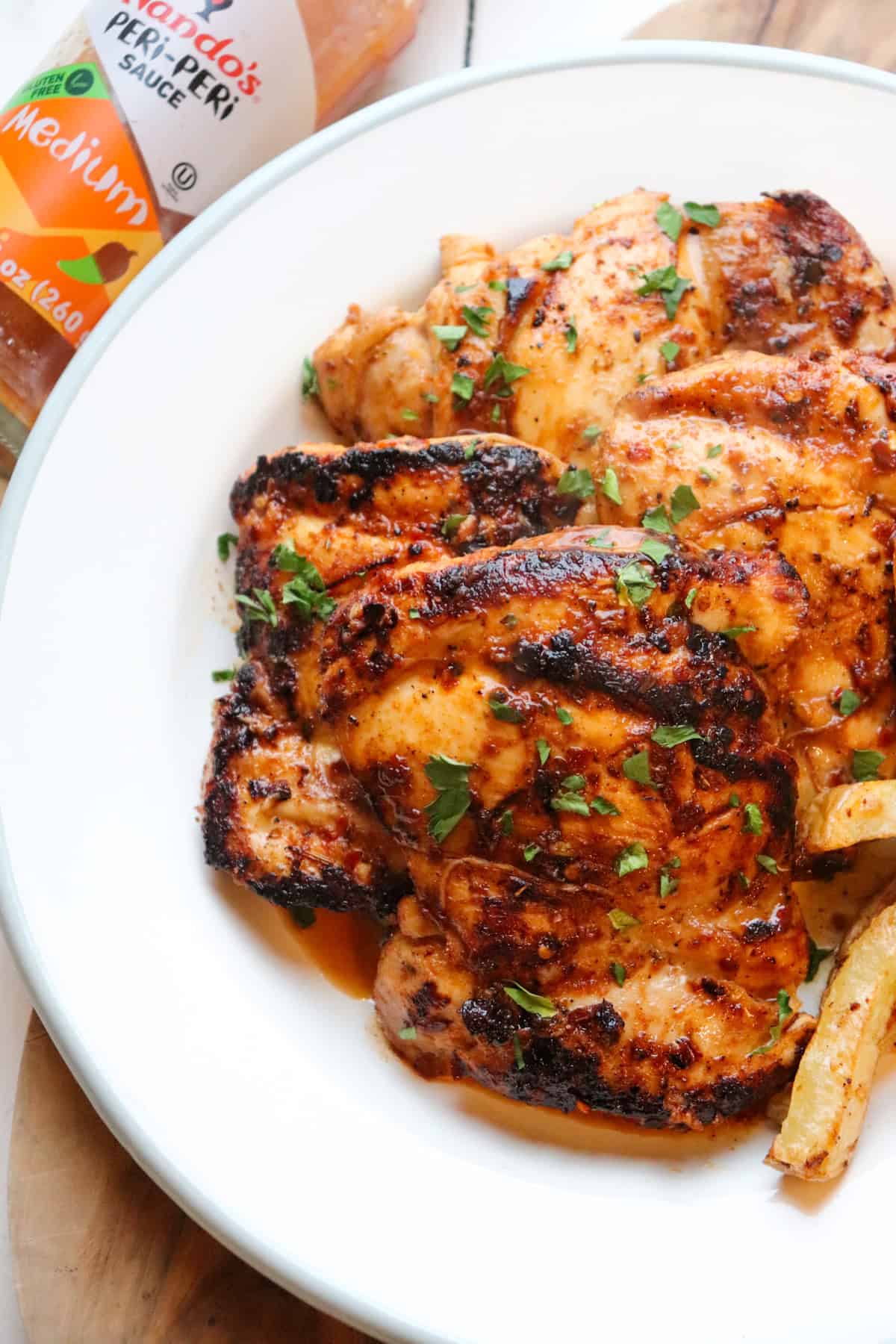 a platter of seasoned chicken thighs with nandos sauce in the background.