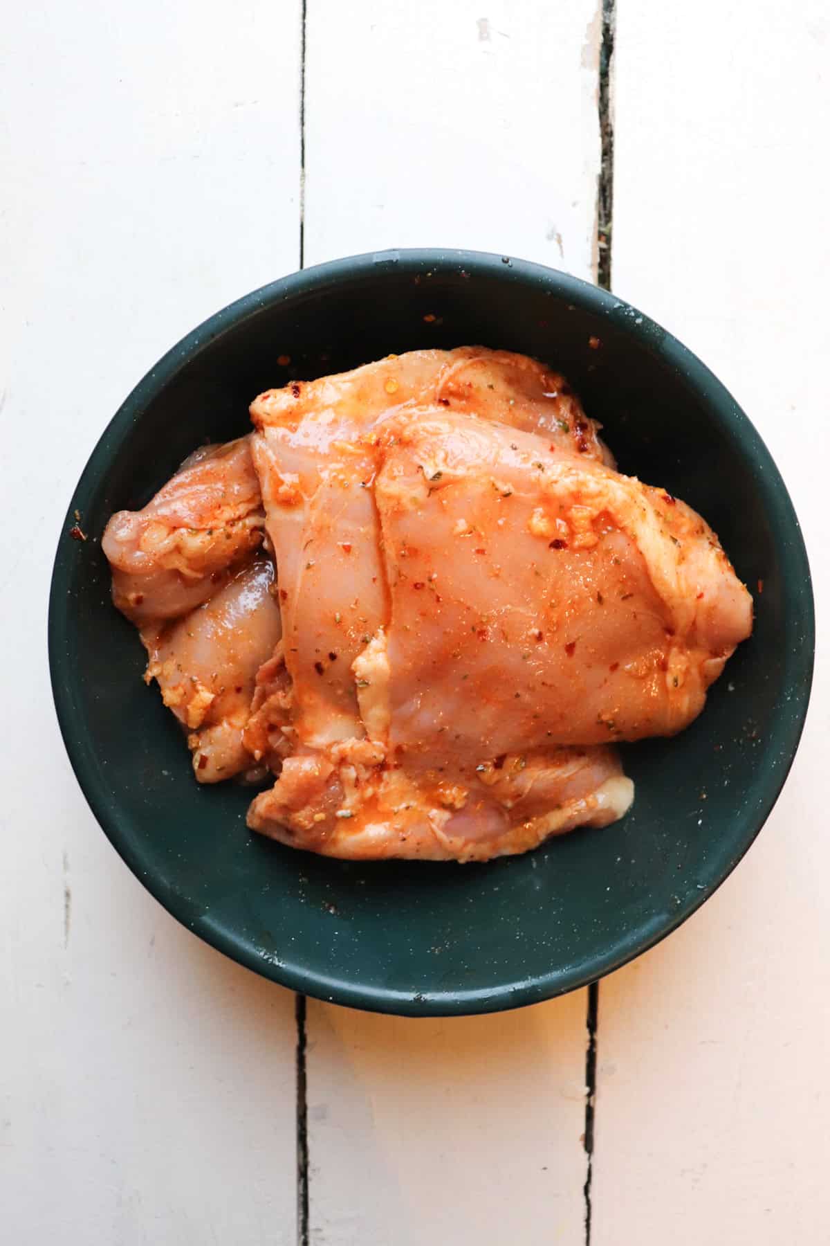 chicken covered in seasoning in a green bowl.