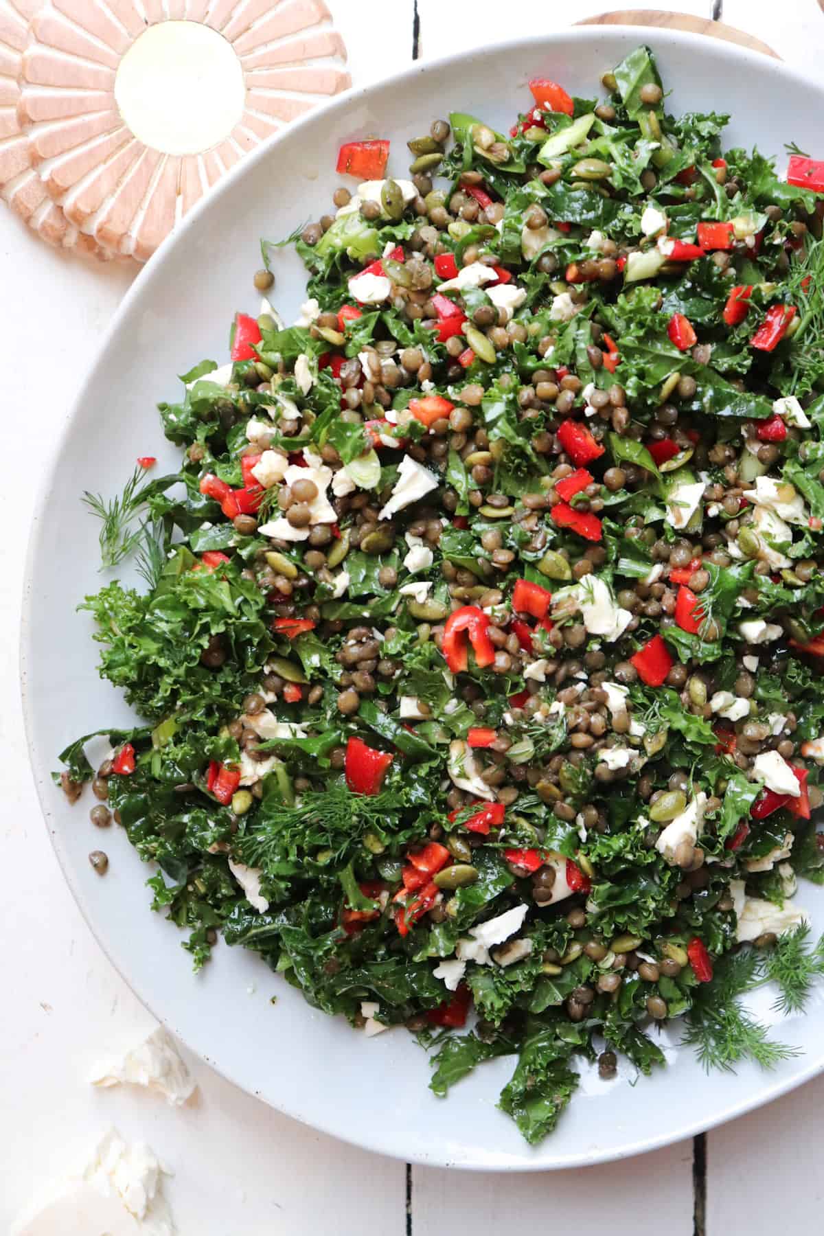 lentil kale salad on a white plate with decorative coasters on the side.