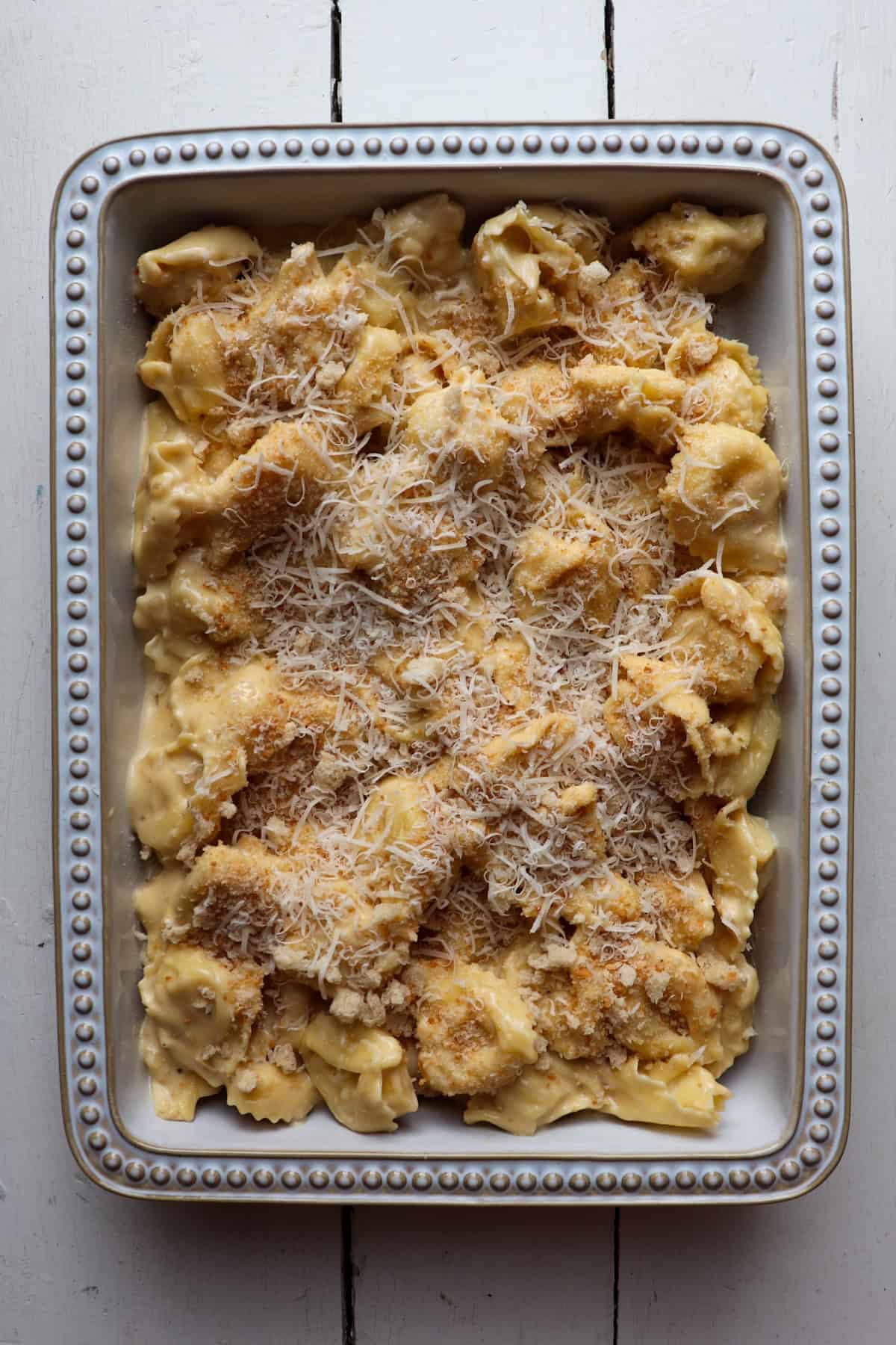 tortellini added to a casserole dish and topped with shredded cheese and breadcrumbs.