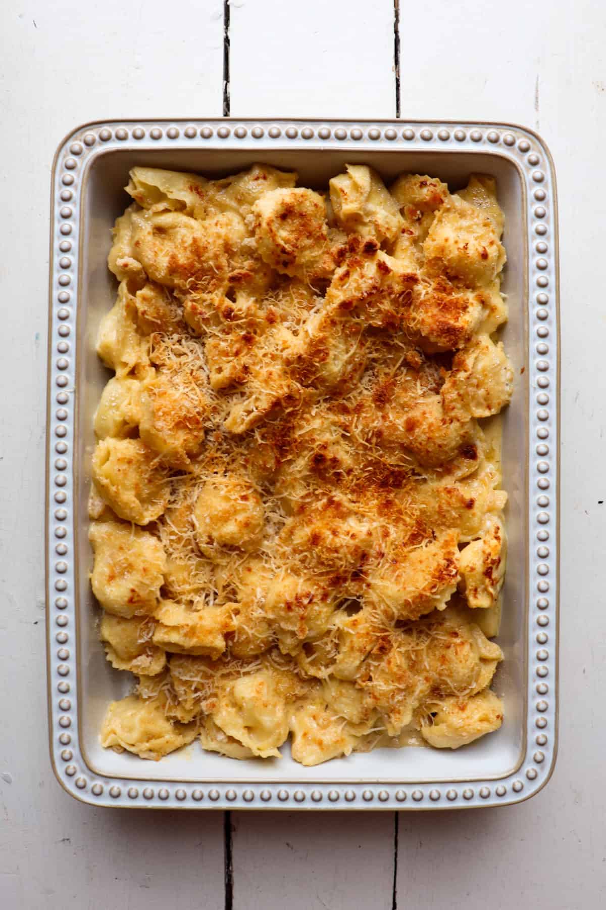 tortellini added to a casserole dish and topped with shredded cheese and breadcrumbs and baked in the oven.