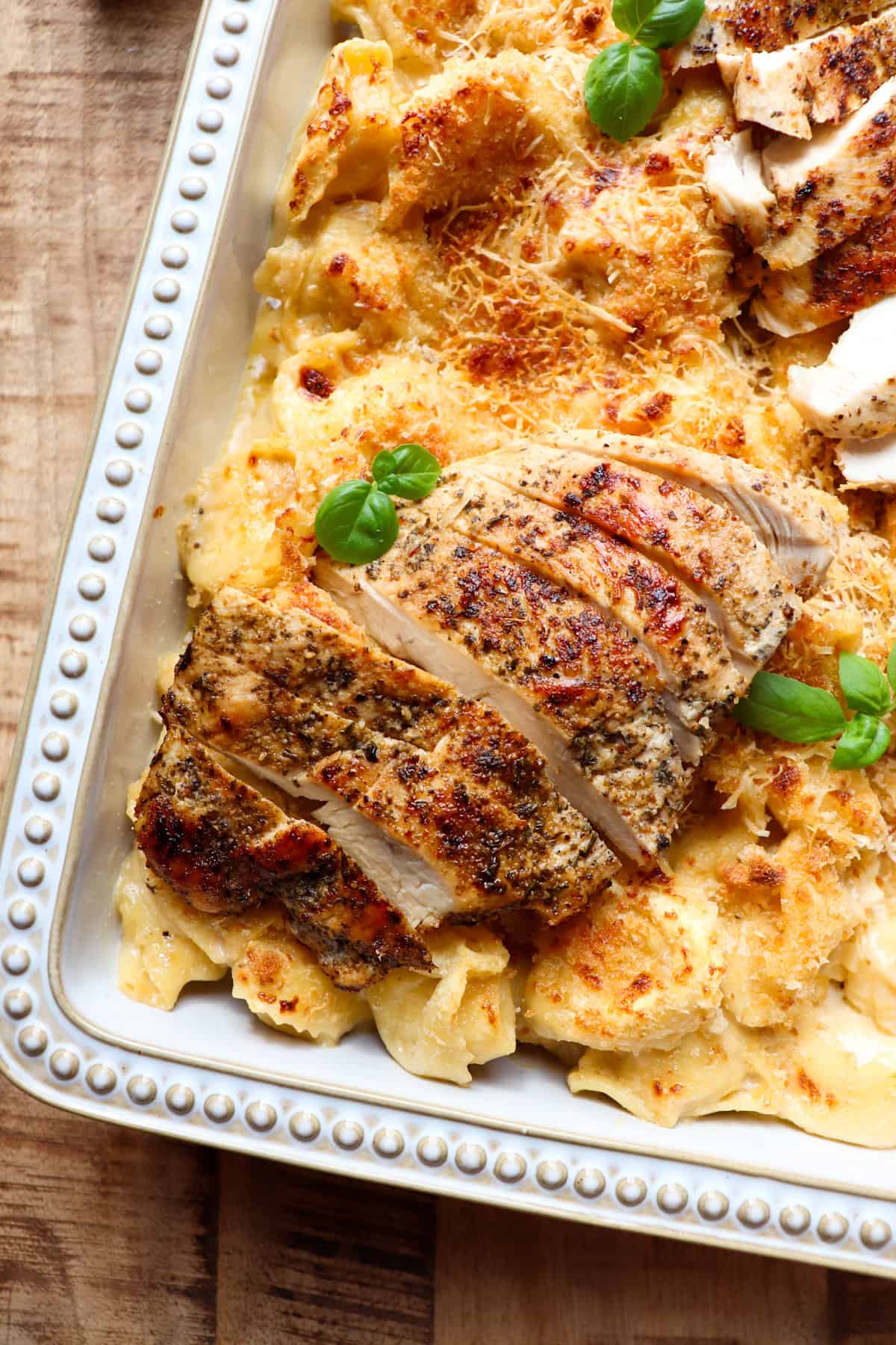 sliced chicken on top of a casserole dish of tortellini that have been baked in the oven.