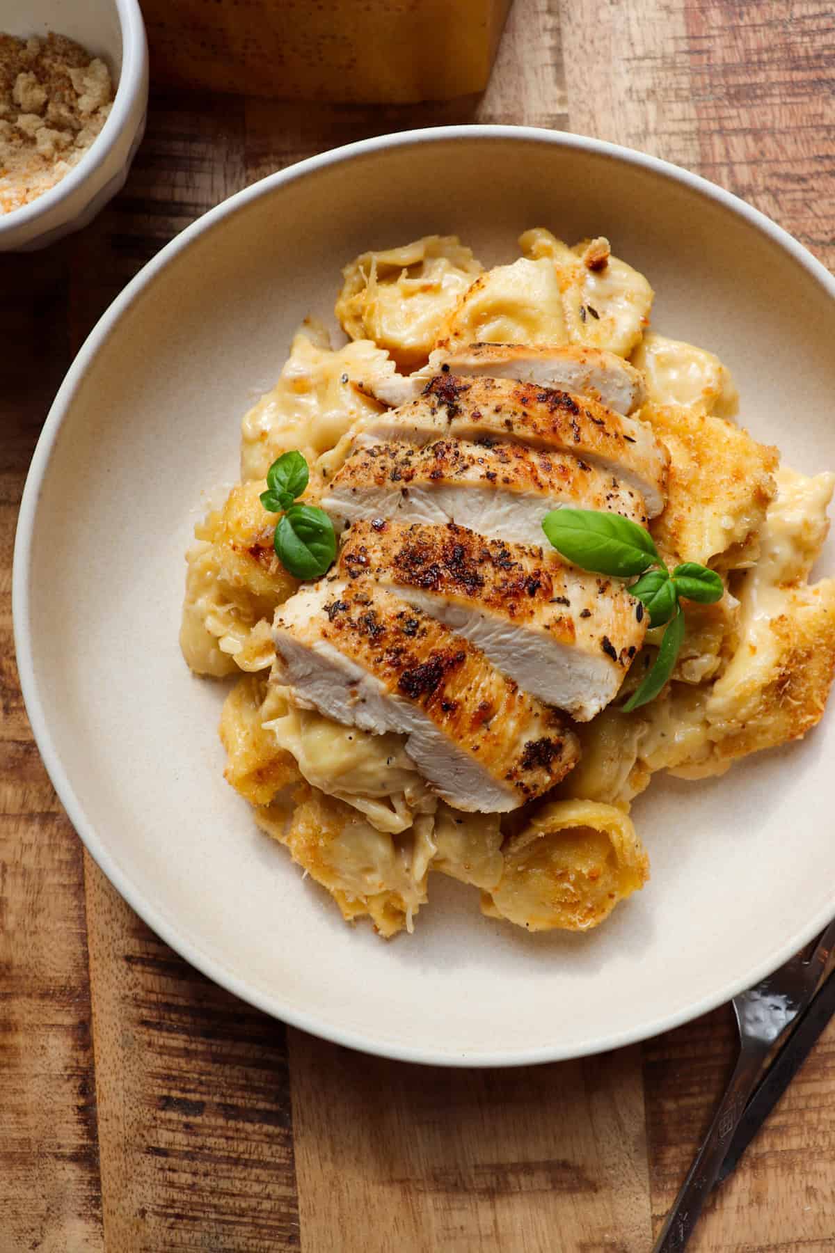 A plate of tortellini pasta with chicken and herbs on it.