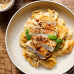 Sliced chicken and tortellini pasta with parmesan and basil for garnish.