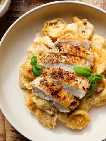 Sliced chicken and tortellini pasta with parmesan and basil for garnish.