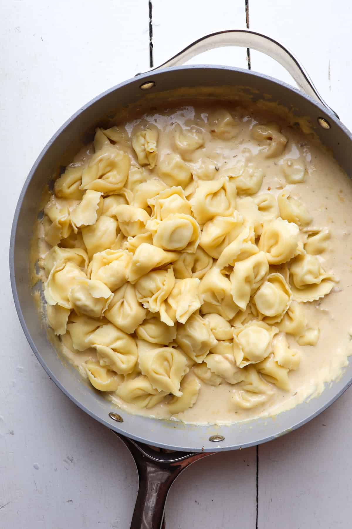 A pan filled with tortellini pasta and alfredo on a white table.