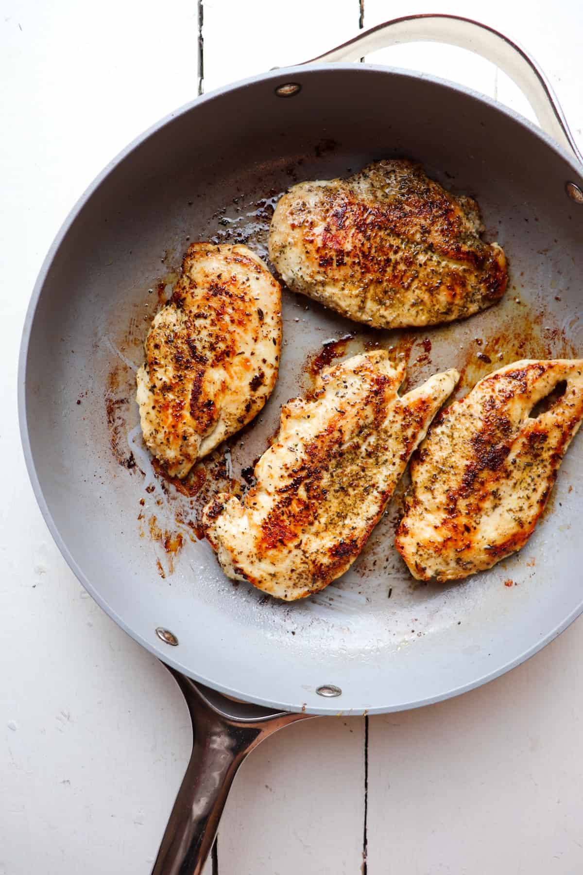 Four pieces of chicken in a skillet on a white table.