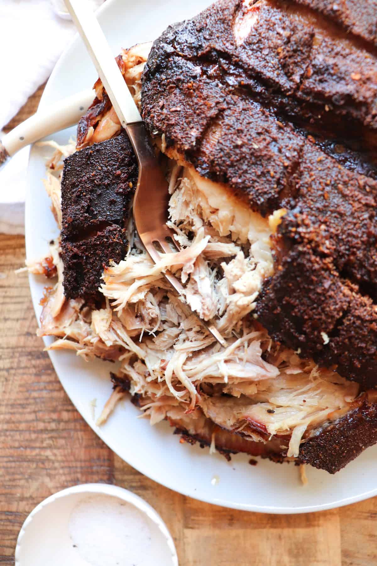 pork shoulder on a serving plate being shredded with a fork.