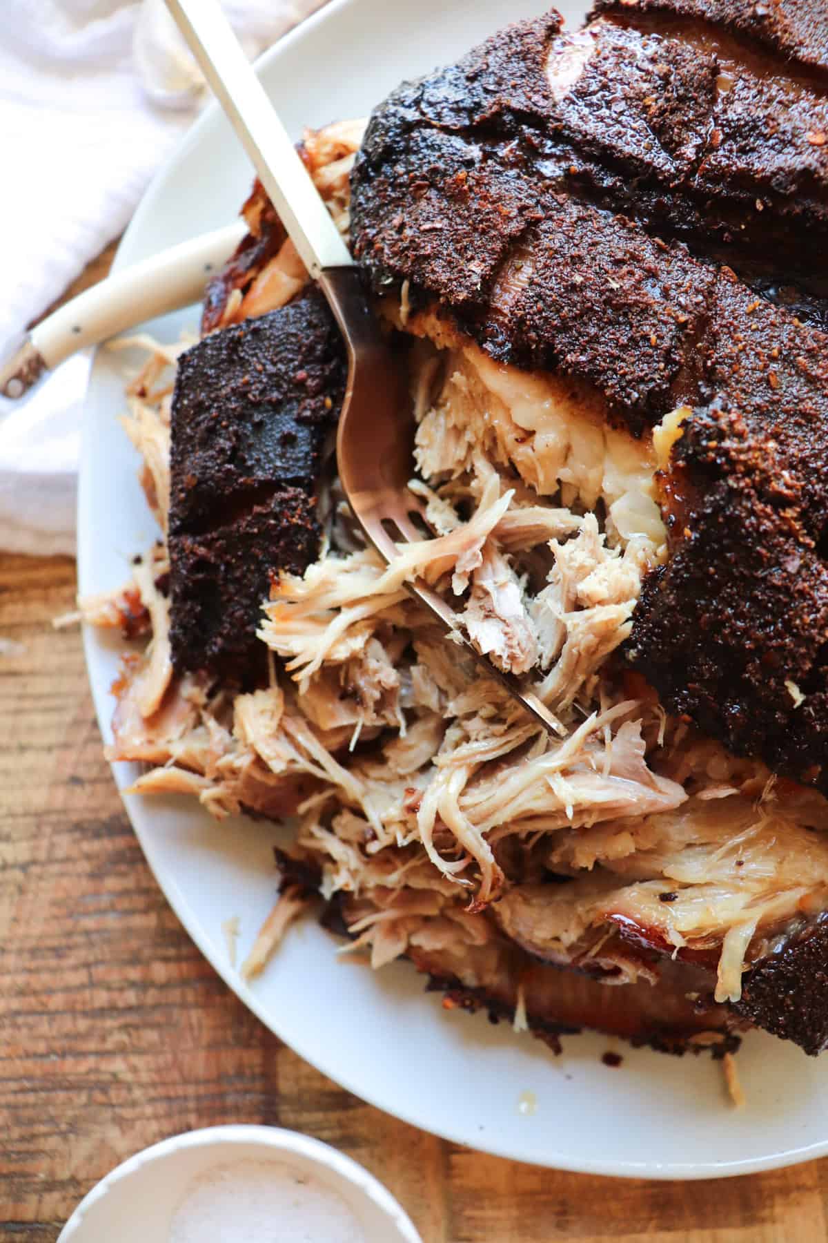 pork shoulder on a serving plate being shredded with a fork.