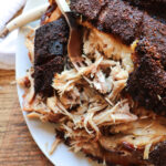 pork shoulder on a serving plate being shredded with a fork.
