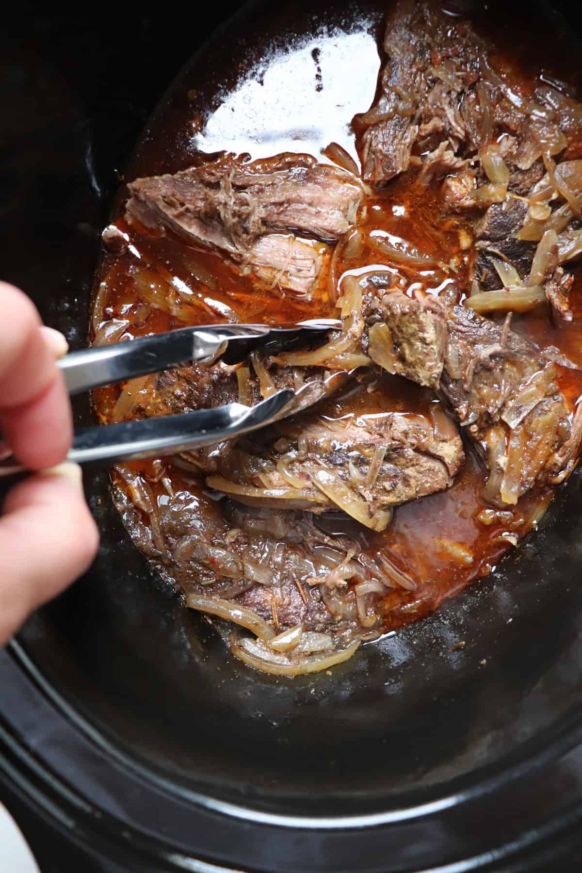 tongs breaking up the meat in the crock pot.