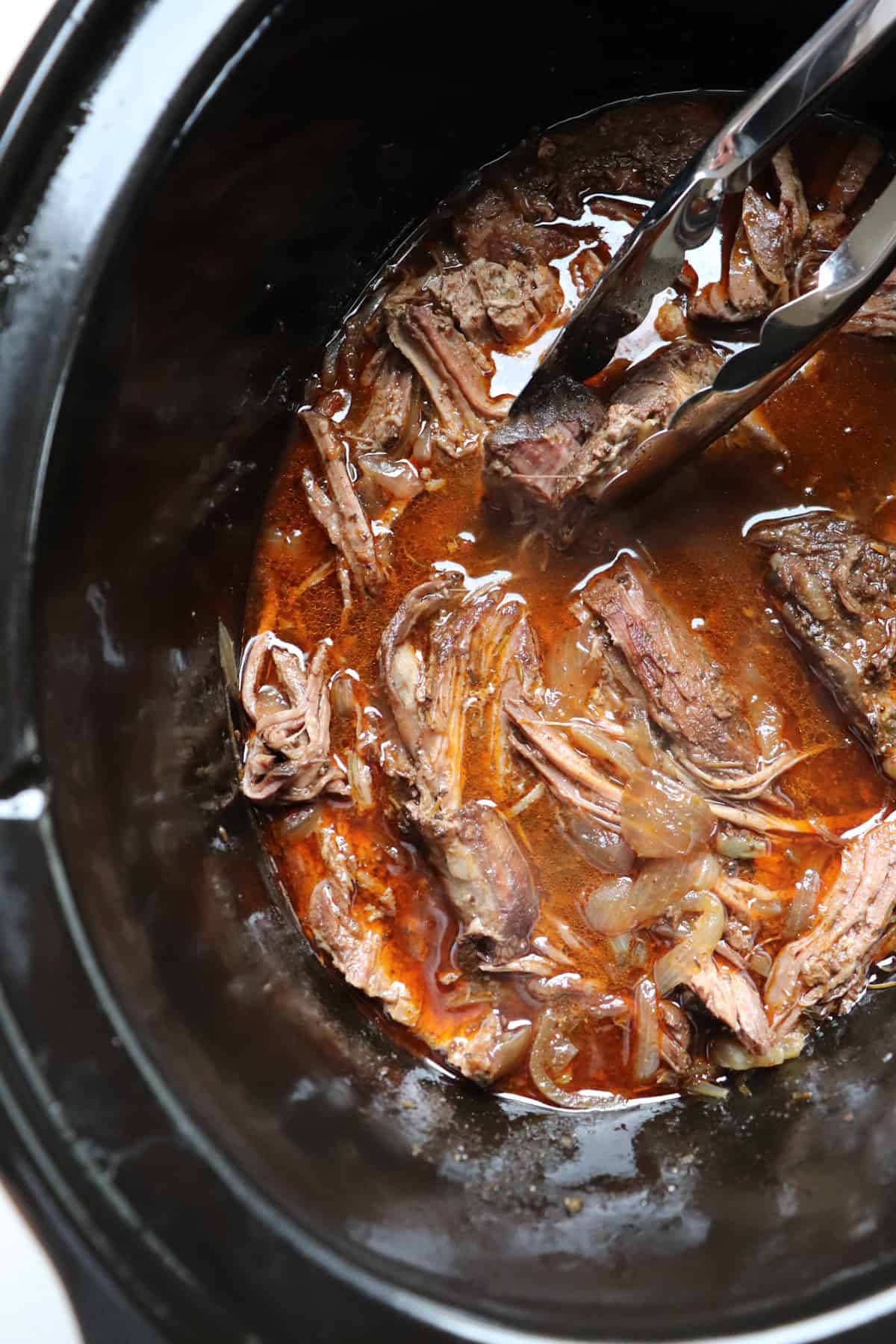 tongs grabbing sirloin meat from a crock pot.