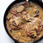 A skillet filled with salisbury steak patties and mushrooms up close.