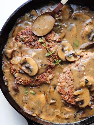 A skillet filled with salisbury steak patties and mushrooms up close.