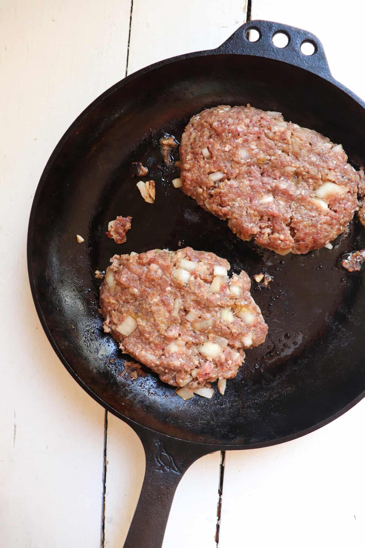two venison salisbury steak patties in a cast iron skillet.