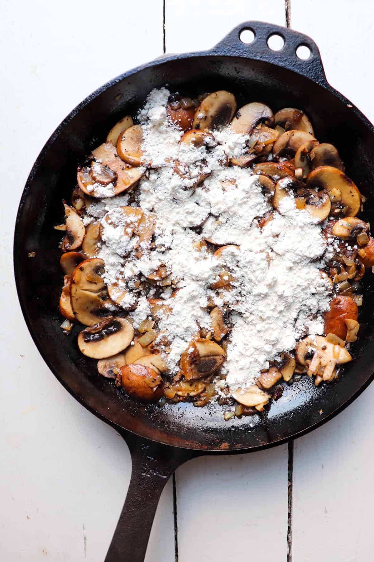 flour sprinkled on top of mushrooms in skillet.