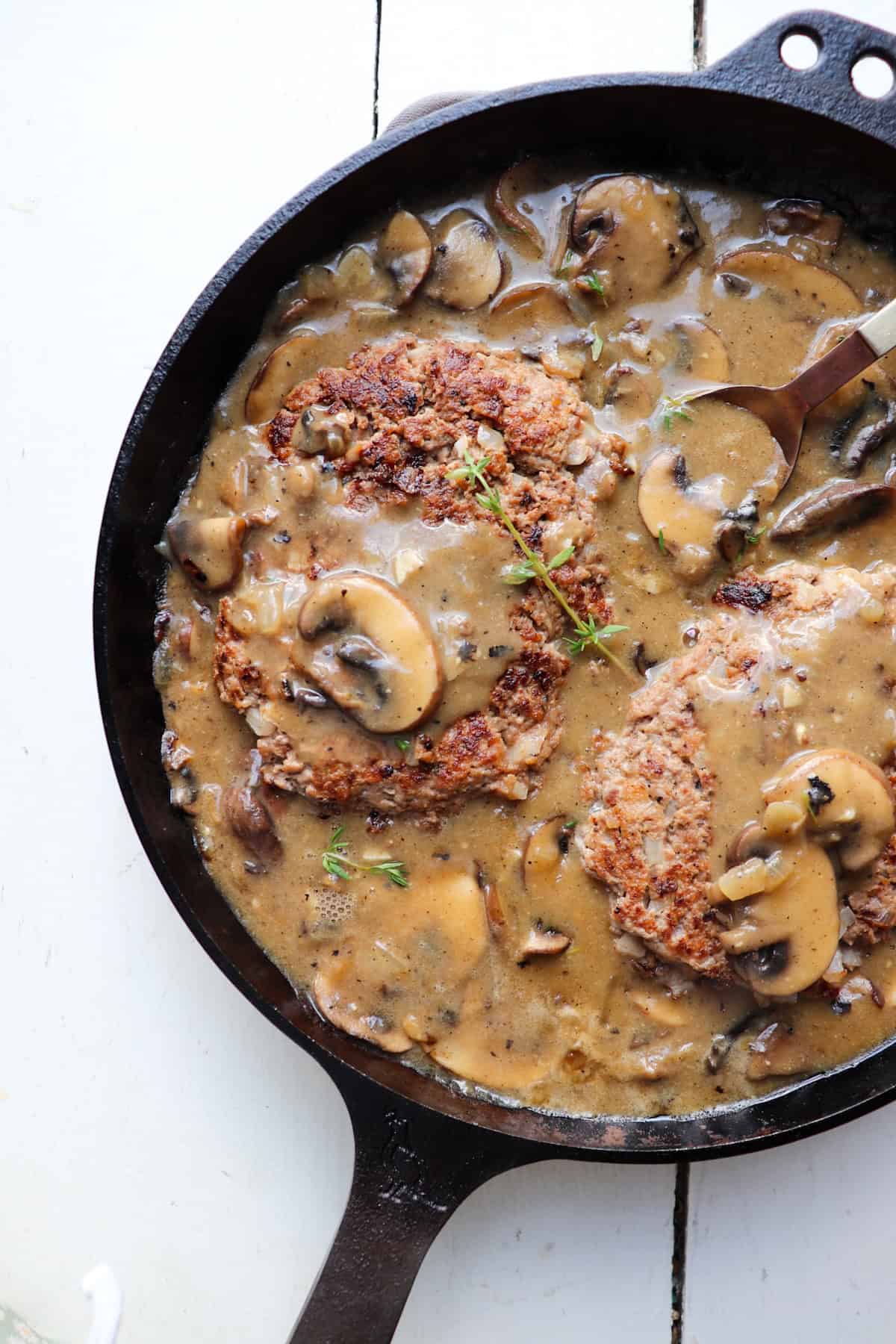 A skillet filled with salisbury steak patties and mushrooms.