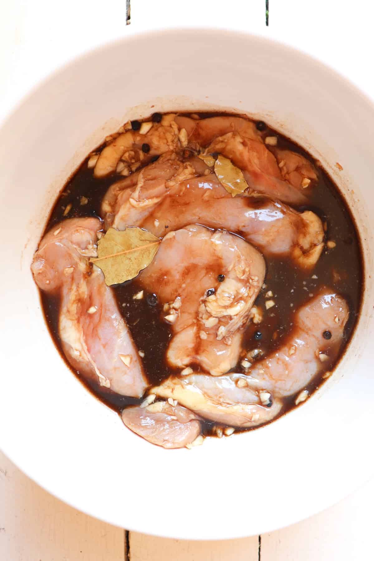 chicken thighs in adobo marinade in a white bowl.