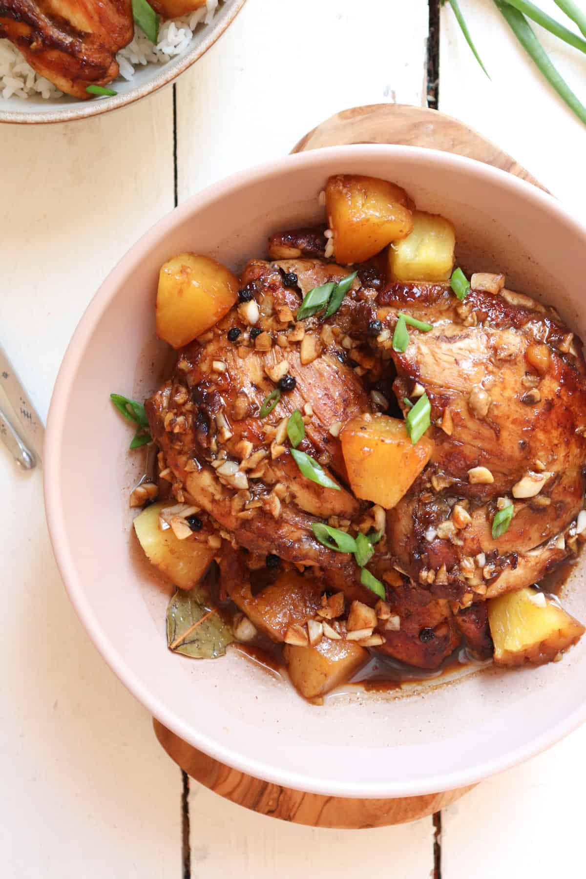 chicken adobo with pineapple plated in a low tan bowl garnished with green onions.