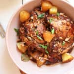 chicken adobo with pineapple plated in a low tan bowl with slcied green onions on top.