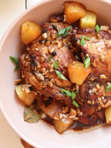 chicken adobo with pineapple plated in a low tan bowl with slcied green onions on top.