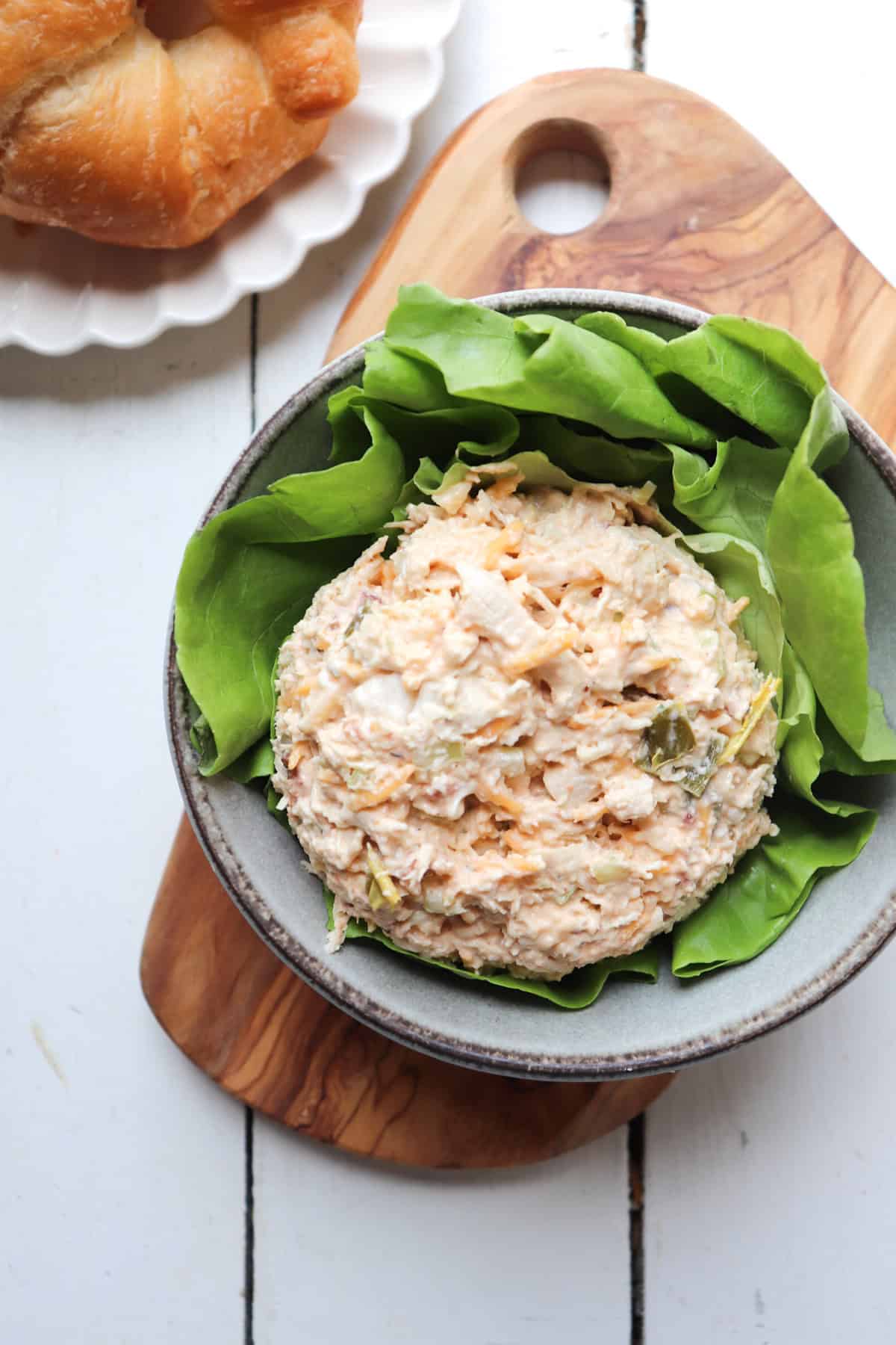 scoop of chicken salad on a bed of lettuce with a croissant in the background.