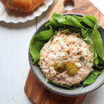 scoop of chicken salad with pickled jalapenos on top on a bed of lettuce with a croissant in the background.