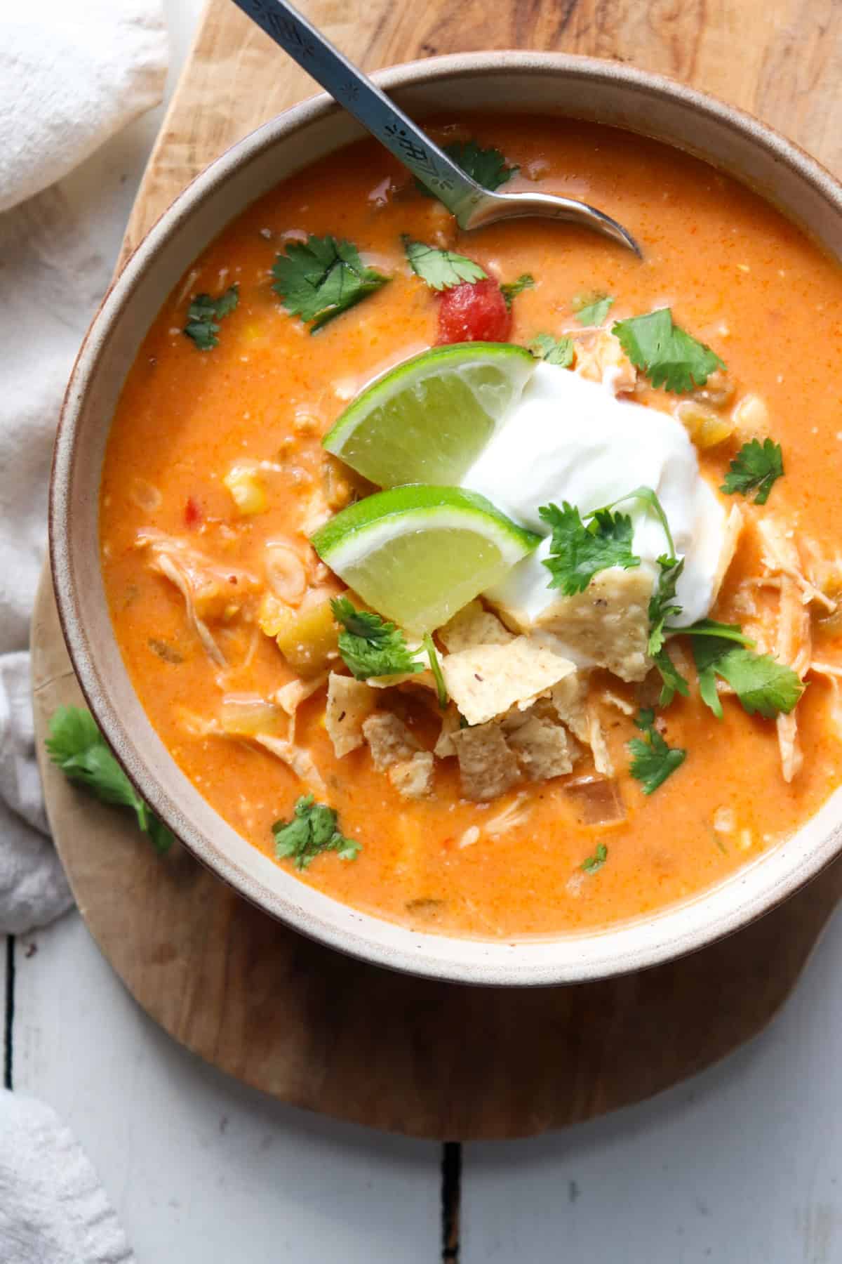 bowl of creamy chicken enchilada soup with garnishes with a spoon in the bowl.