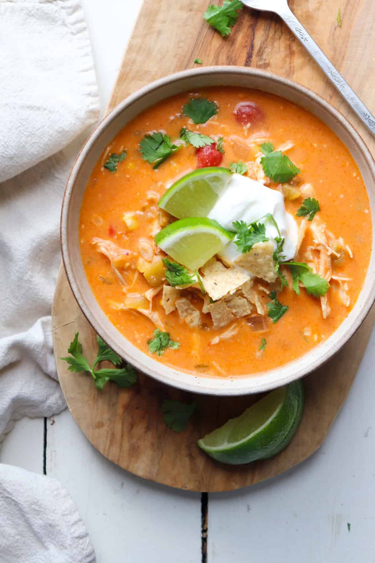 bowl of creamy chicken enchilada soup with garnishes on a wooden board.