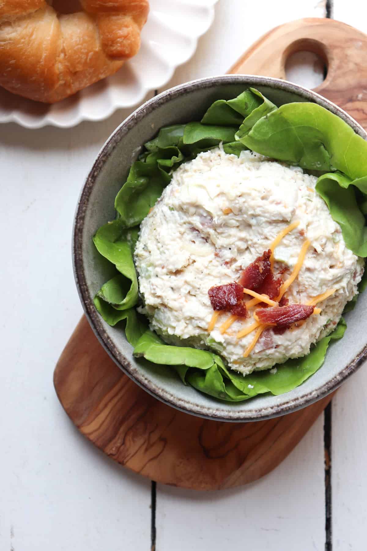 scoop of chicken salad on butter lettuce in a bowl topped with bacon and cheese. 