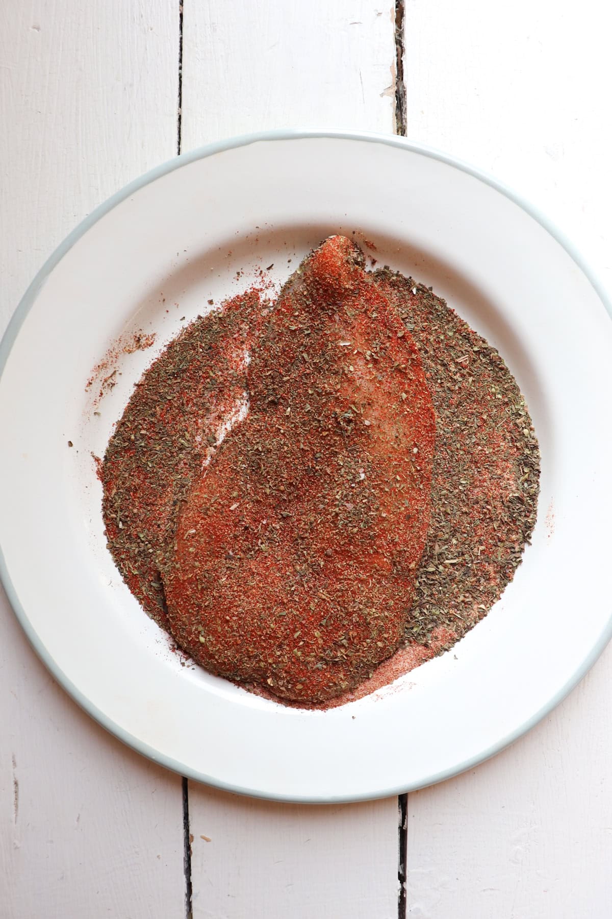 one chicken breast coated in seasoning on a white plate.