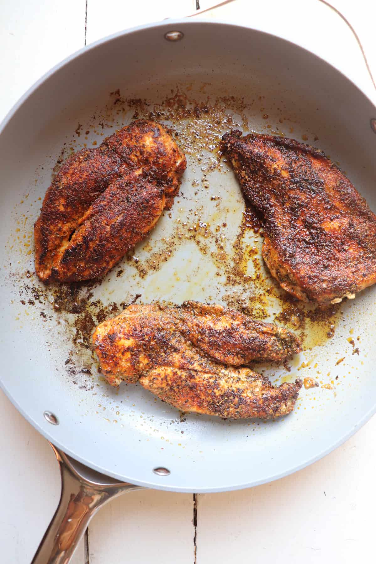 three pieces of seasoned chicken in a skillet.