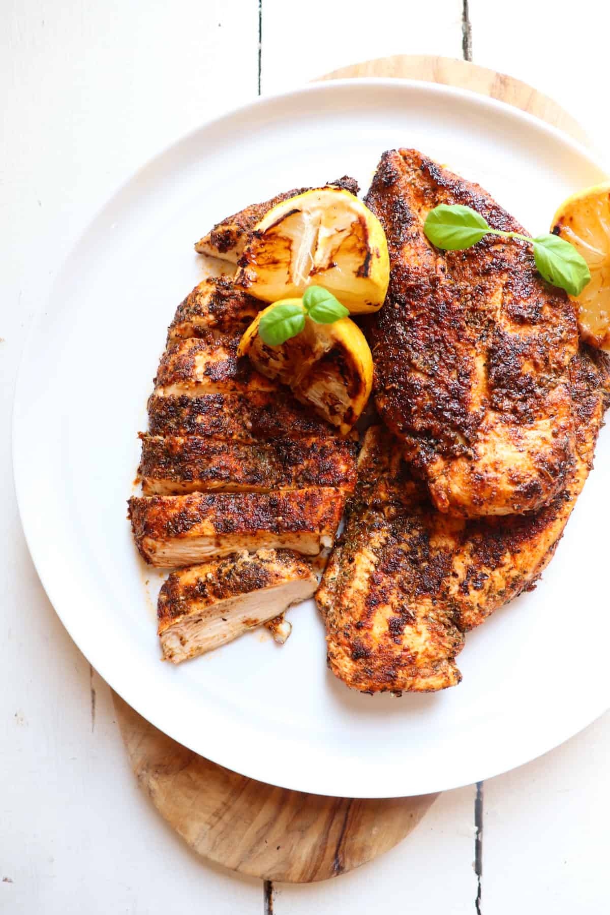 herb crusted chicken on a white plate with lemons and basil as garnish.