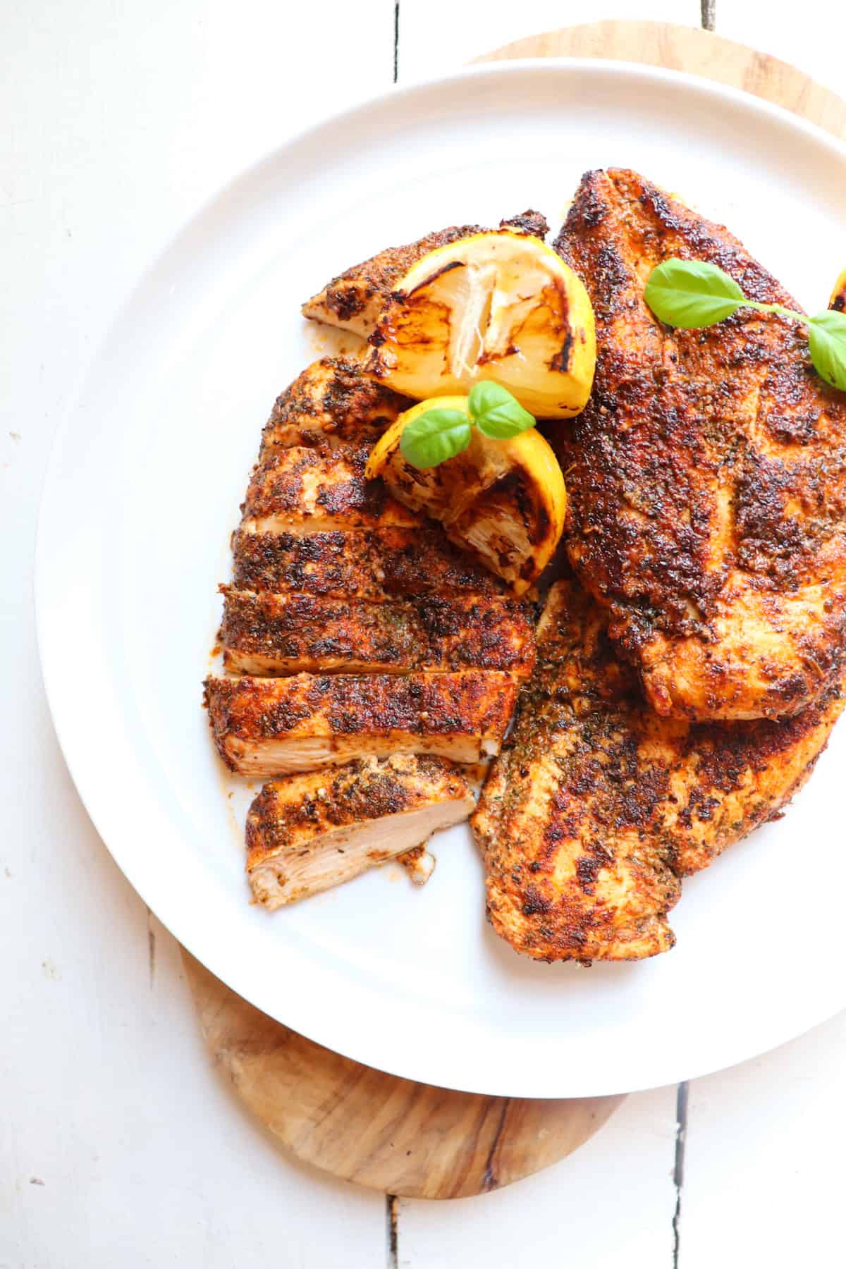 herb crusted chicken on a white plate with lemons and basil as garnish.