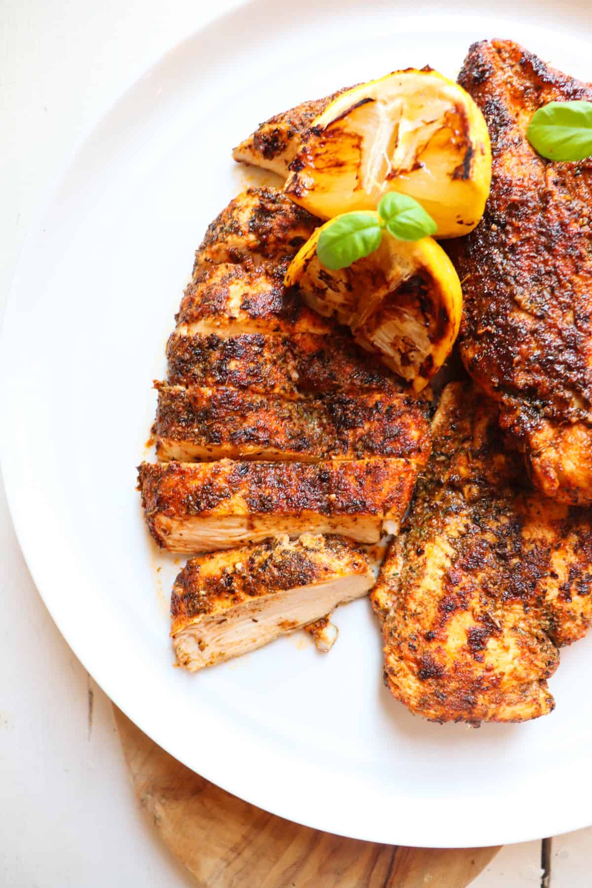 herb crusted chicken on a white plate with lemons and basil as garnish.
