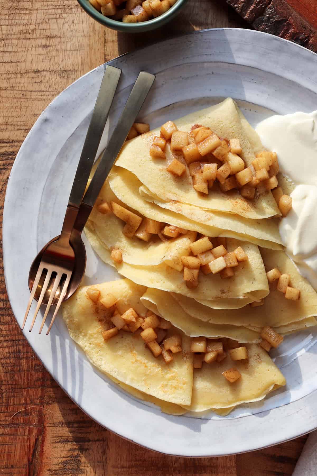 crepes on plate with whipped cream and apples.