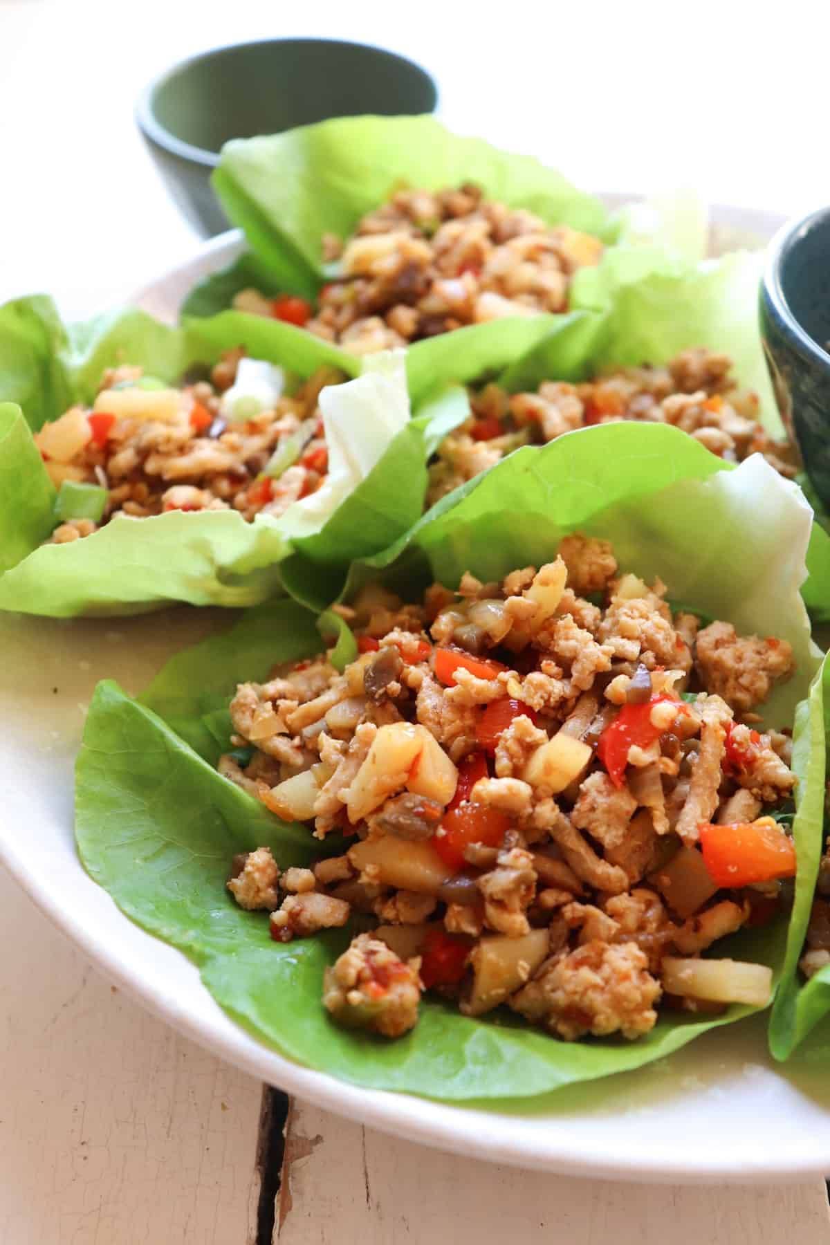 up close photo of a plate of asian chicken lettuce wraps with small bowls in the background.