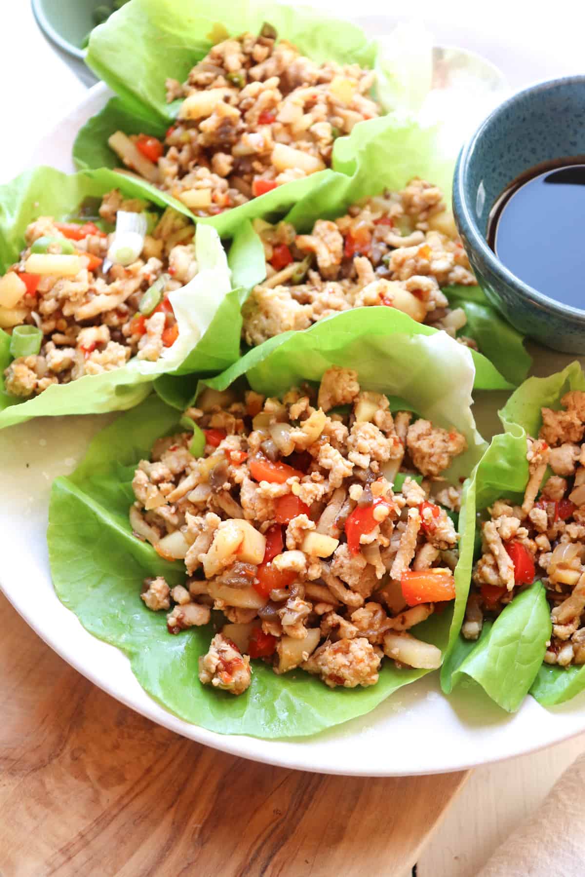 asian chicken lettuce wraps on a plate with small bowl of sauce.