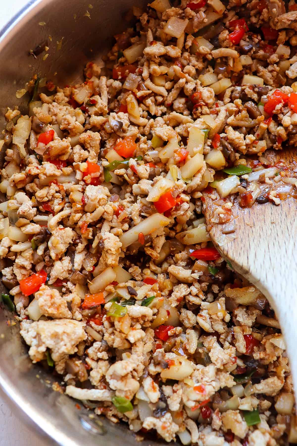 skillet full of finished ground chicken mixture with a wooden spoon stirring.