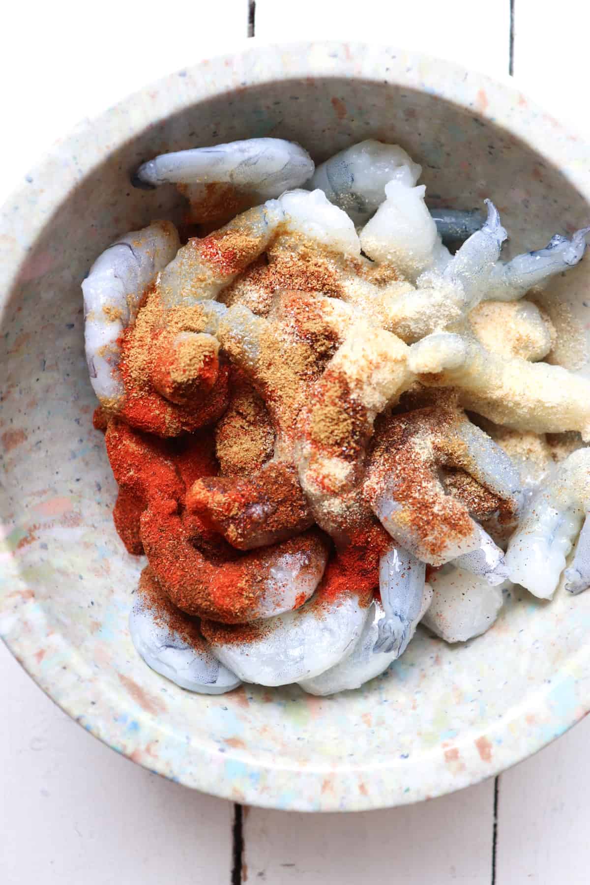 spices and oil added to raw shrimp in a bowl.