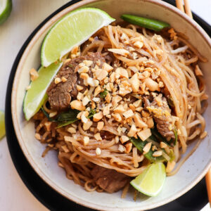bowl of beef pad thai with lime wedges for garnish.