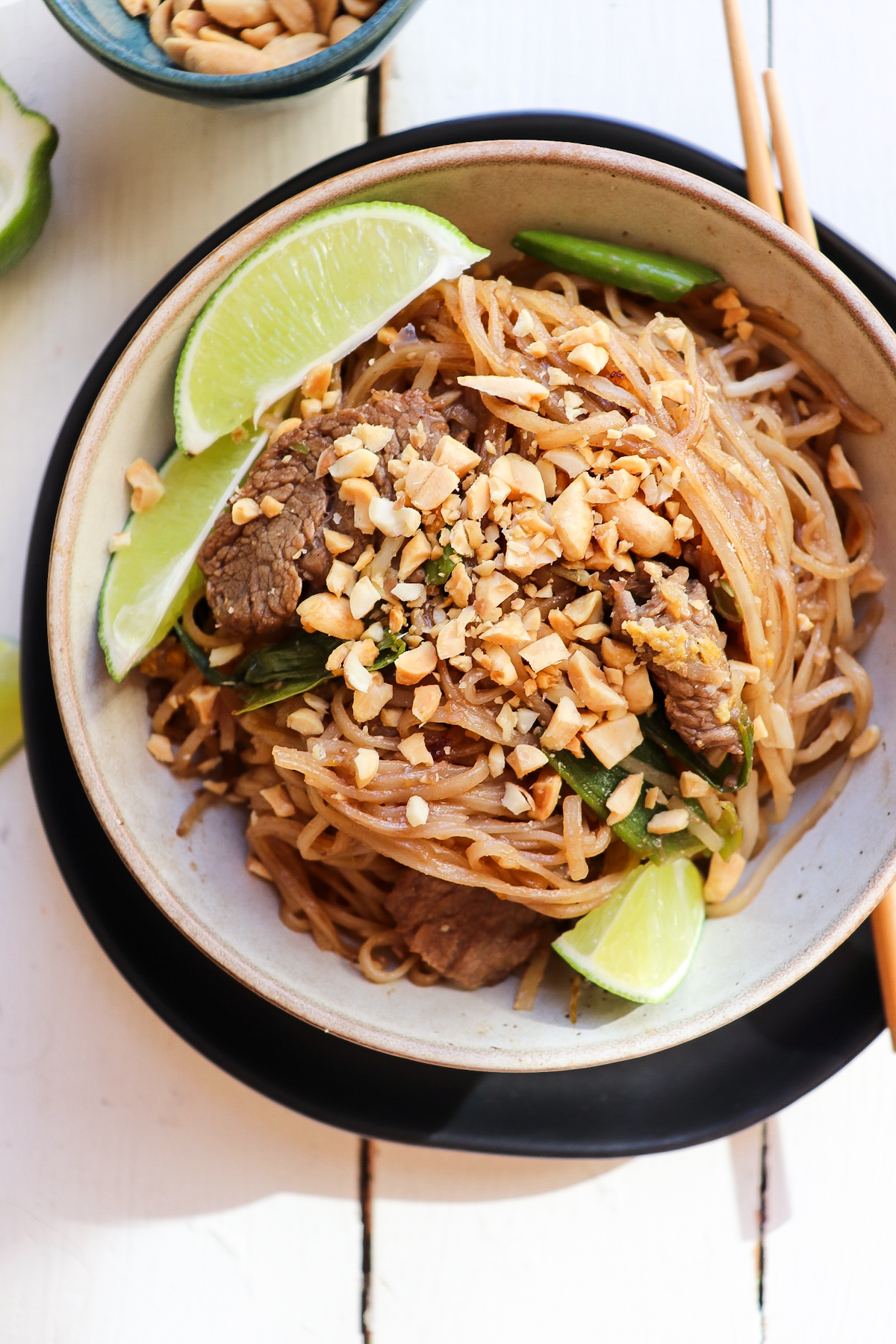 bowl of beef pad thai with lime wedges for garnish.