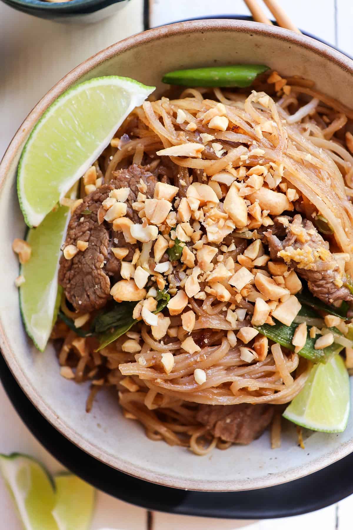 bowl of beef pad thai with lime wedges for garnish.