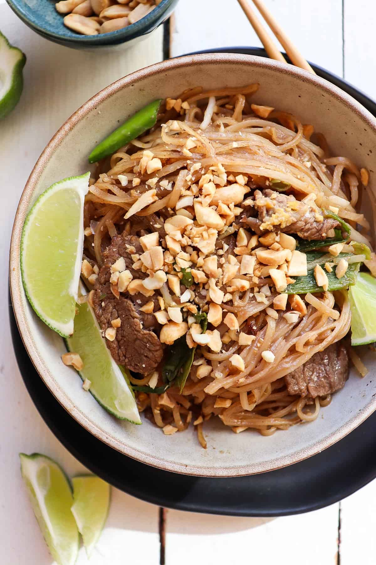 bowl of beef pad thai with lime wedges for garnish.