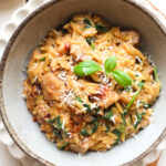 bowl of marry me chicken orzo garnished with parmesan cheese and basil.