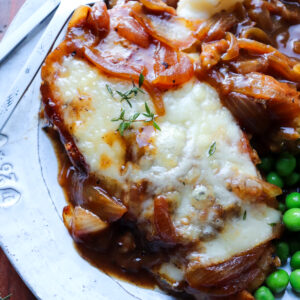 french onion soup chicken on a bed of mashed potatoes with peas on side.