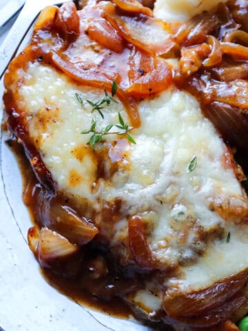 french onion soup chicken on a bed of mashed potatoes with peas on side.